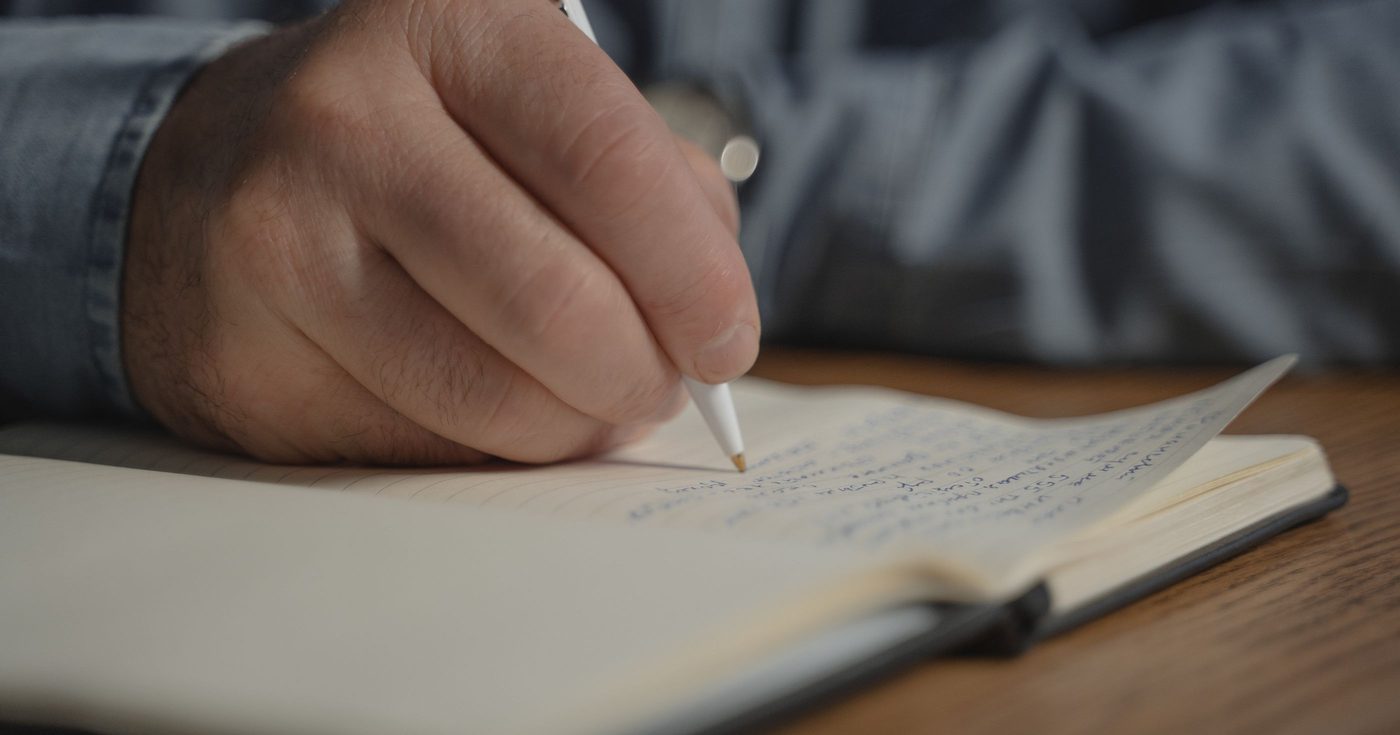 A hand writing with a pen in a notebook