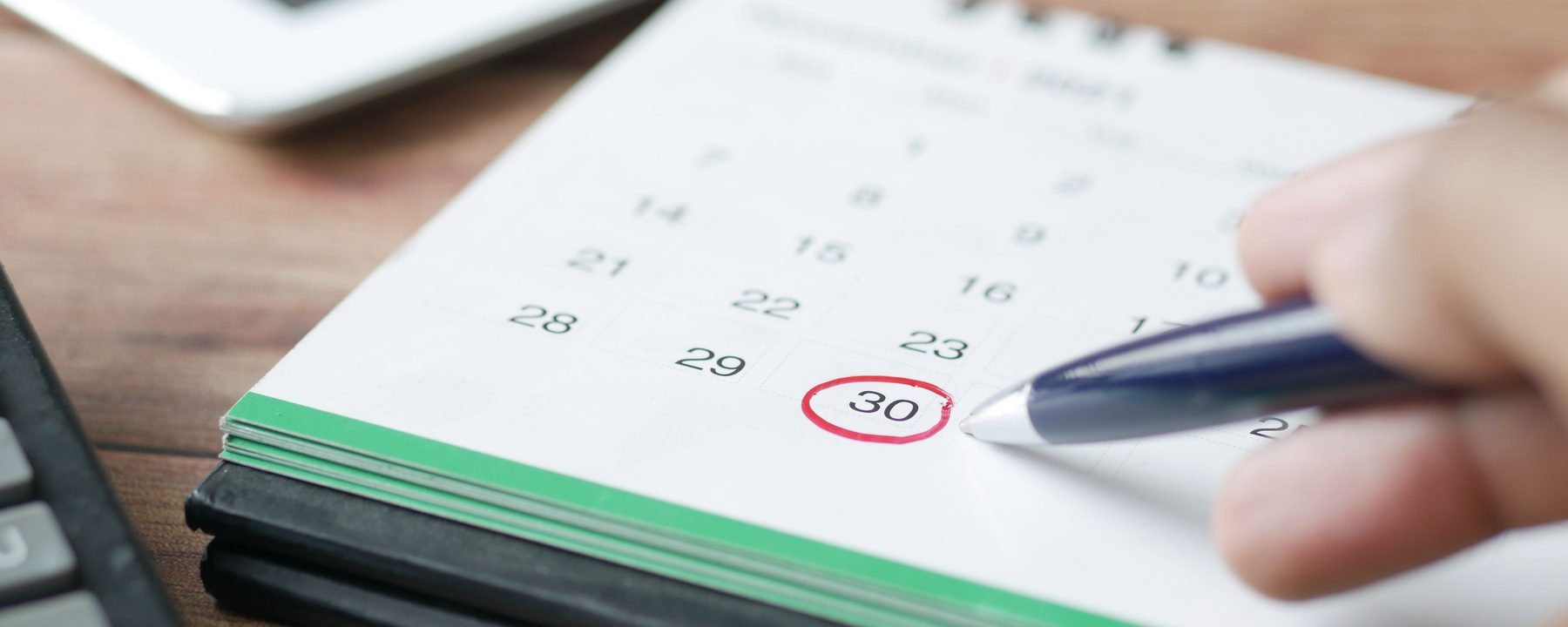 A hand marking a day in a monthly calendar