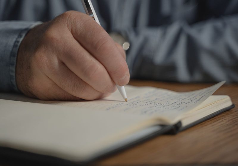 A hand writing with a pen in a notebook