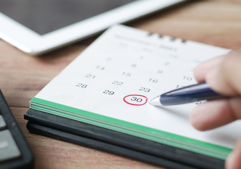 A hand marking a day in a monthly calendar