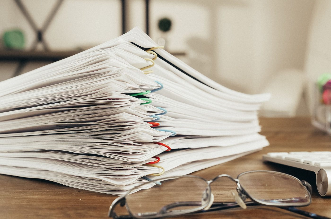 A stack of documents on a desk with a pair of reading glasses